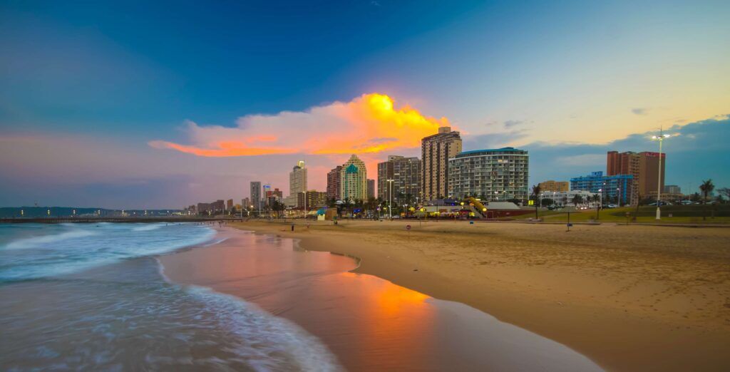 Sandstrand mit kleinen Wellen vor der Skyline von Durban bei Sonnenuntergang