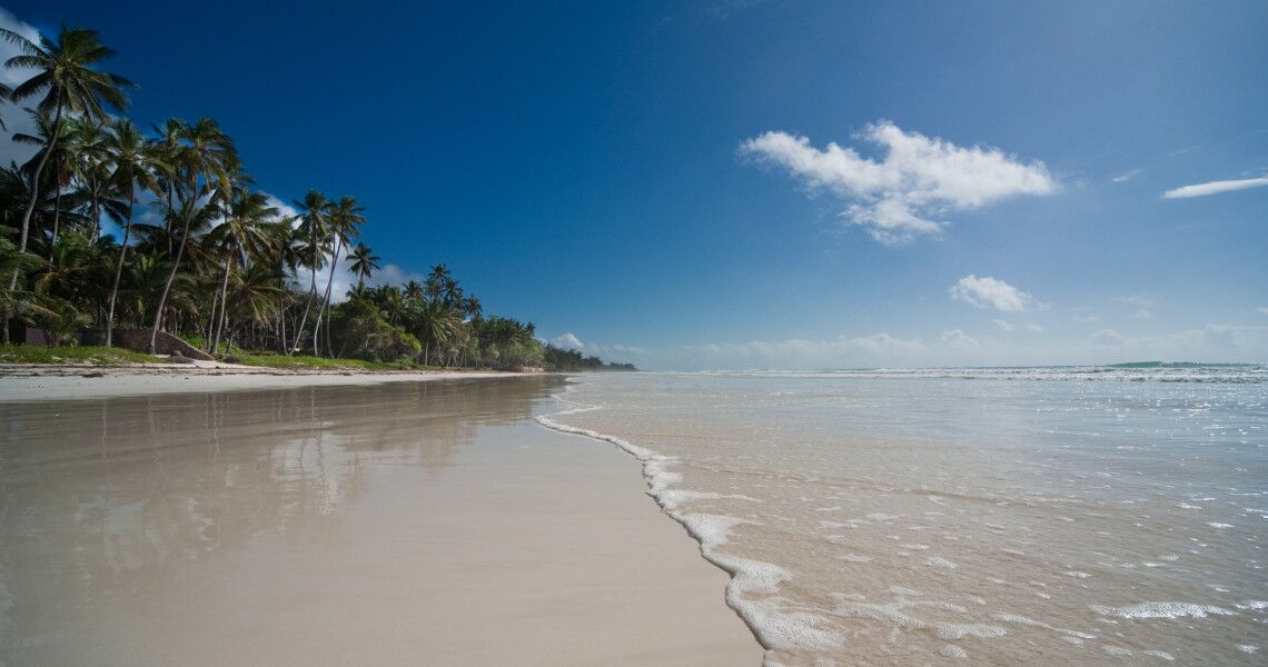 Weißer Sandstrand von Diani Beach mit Palmen auf einer Seite und dem Indischen Ozean auf der anderen