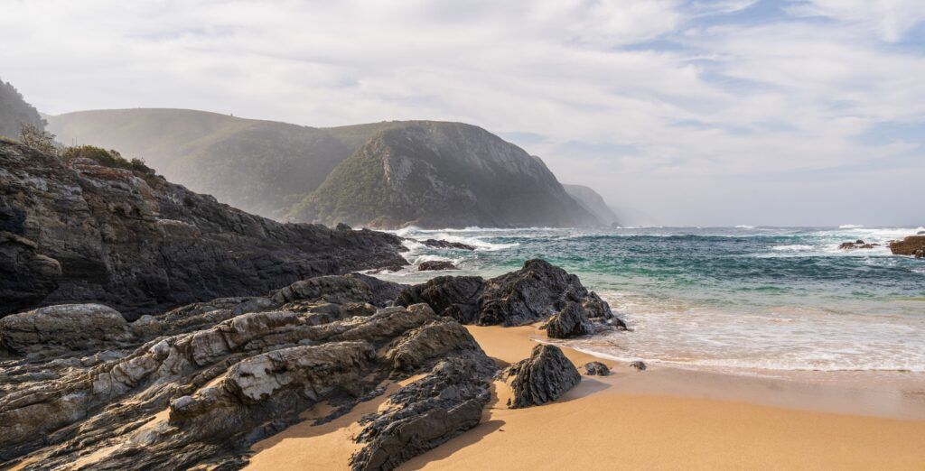 Bucht mit Sandstrand, Wellen und felsiger Küste
