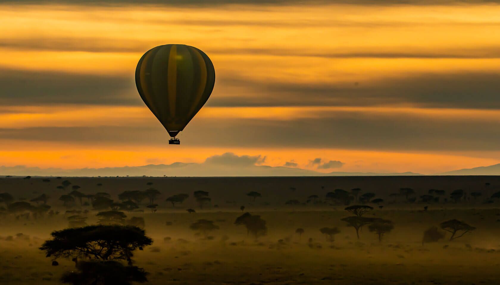 Heißluftballon bei Sonnenuntergang über einer Savanne