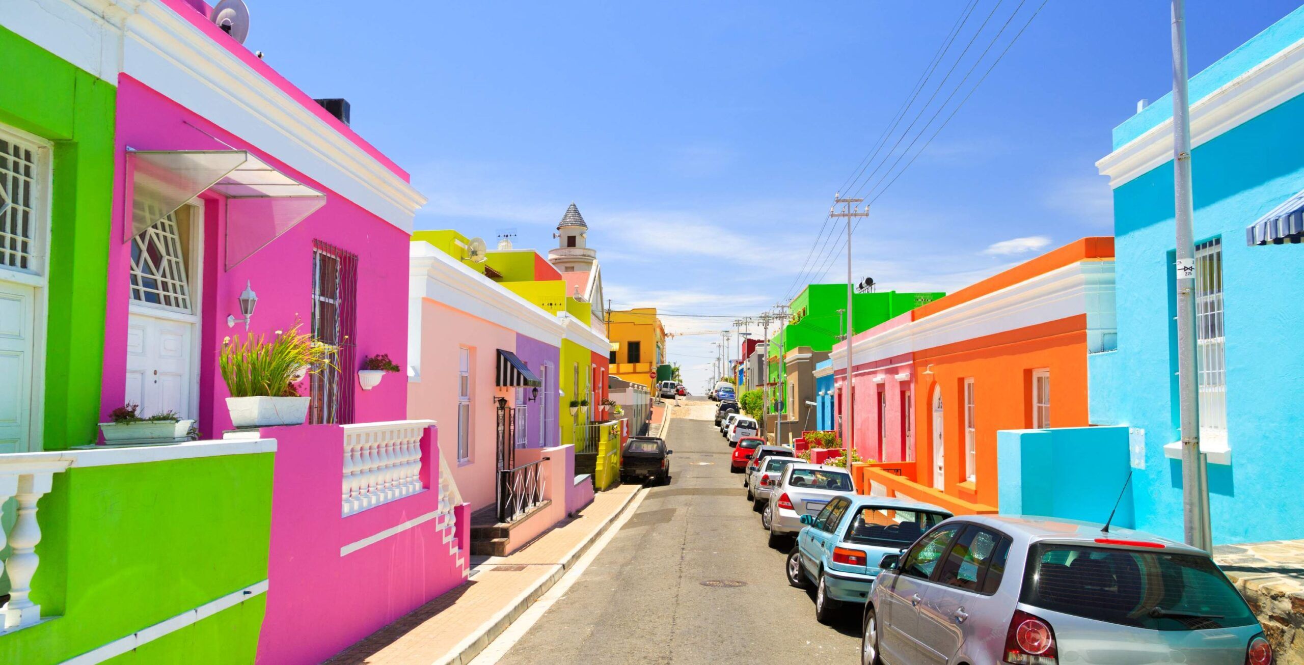 Bo-Kaap mit kleinen bunten Reihenhäusern und geparkten Autos auf der rechten Seite
