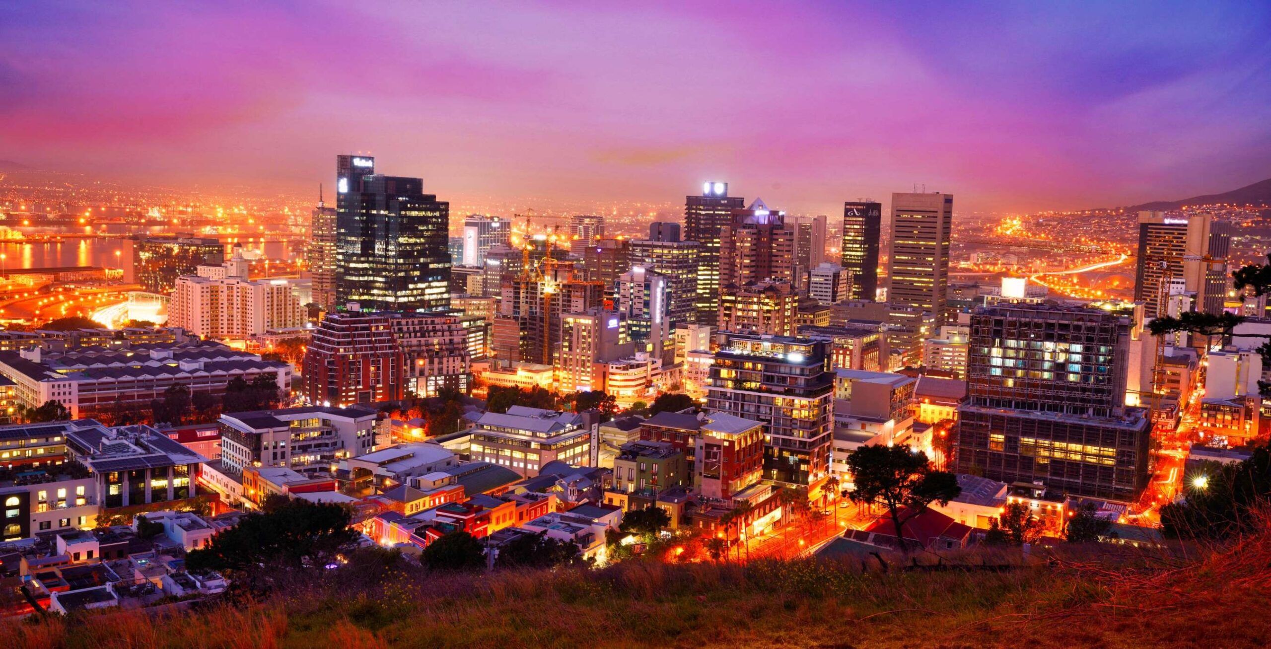 Beleuchtete Kapstadt Skyline bei Nacht bei pink-lilafarbenem Himmel