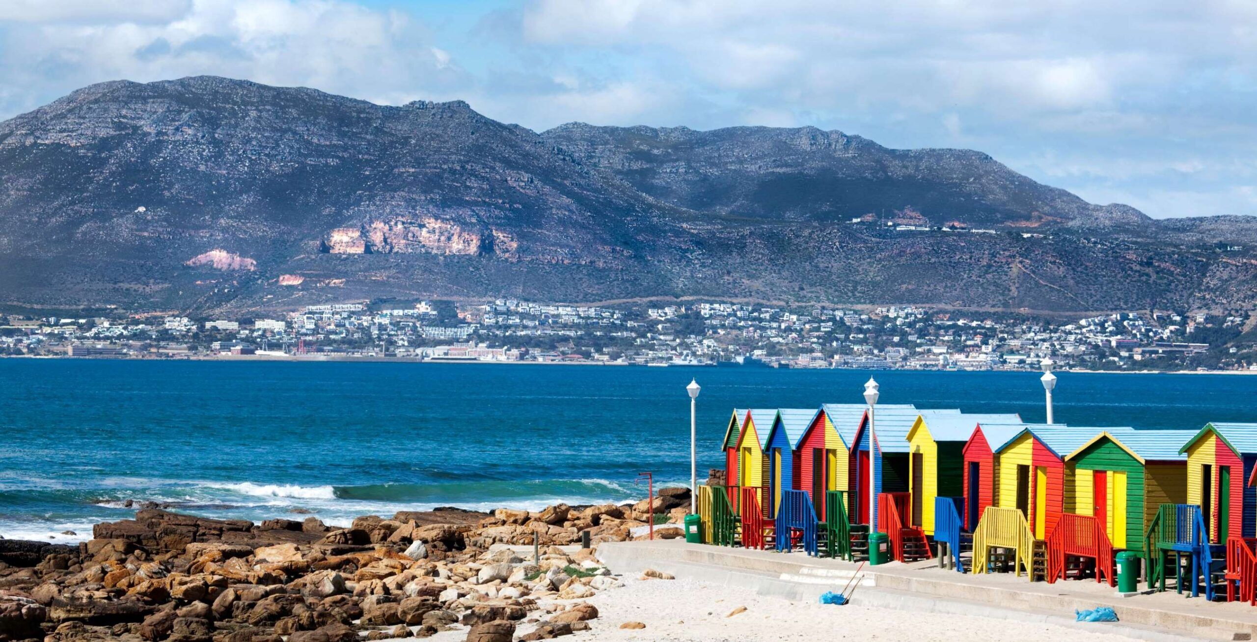 Muizenberg Beach mit kleinen bunten Hütten und dem Meer sowie Bergen im Hintergrund