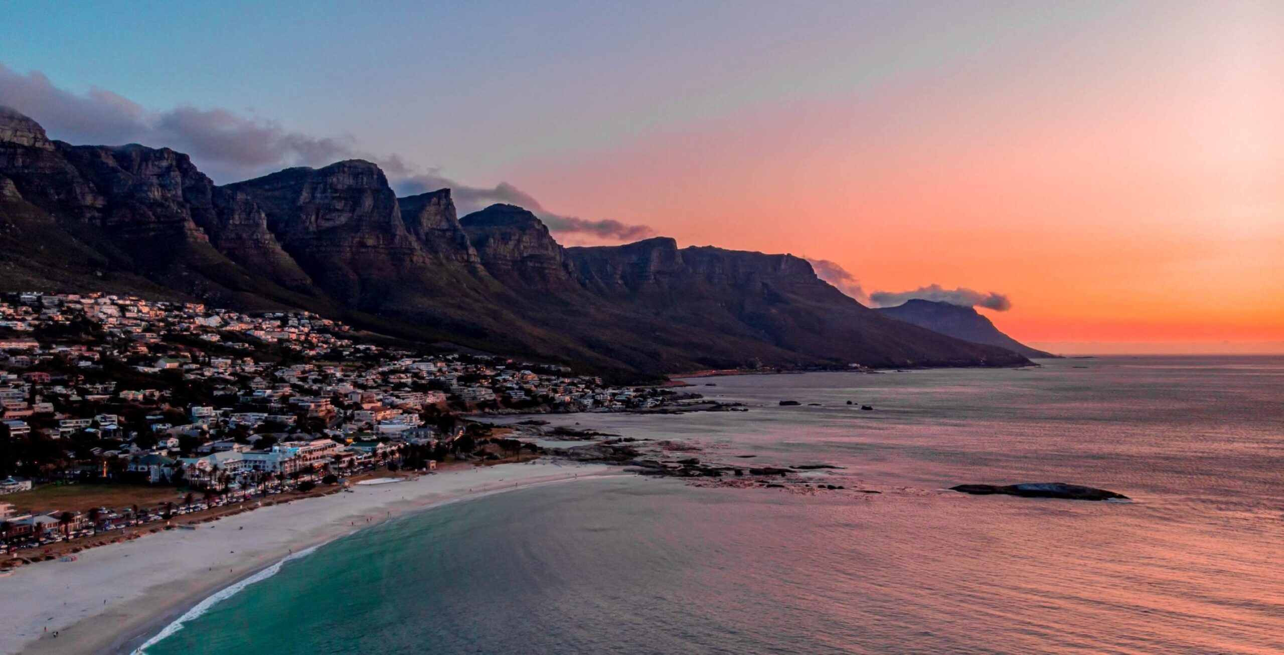 Sandstrand bei Kapstadt bei Sonnenuntergang mit Bergen im Hintergrund