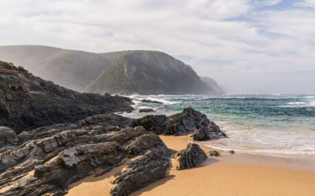 Bucht mit Sandstrand, Wellen und felsiger Küste