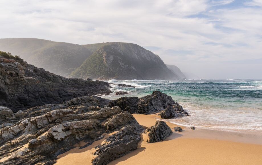 Bucht mit Sandstrand, Wellen und felsiger Küste