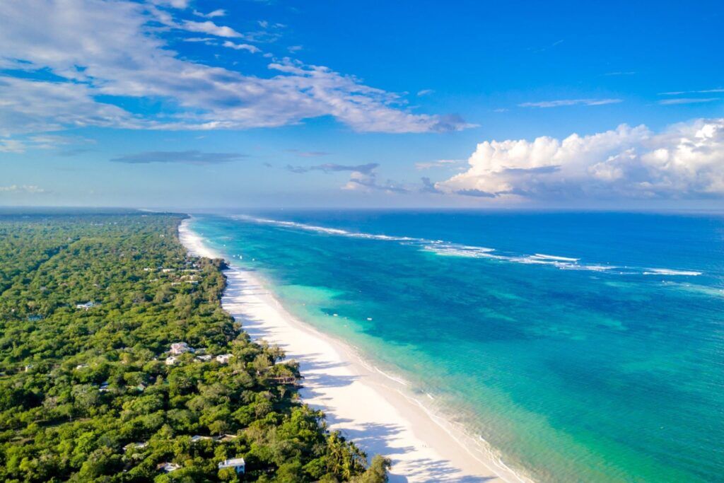 Weißer Sandstrand von Diani Beach mit Bäumen auf einer und dem blauen Meer auf der anderen Seite