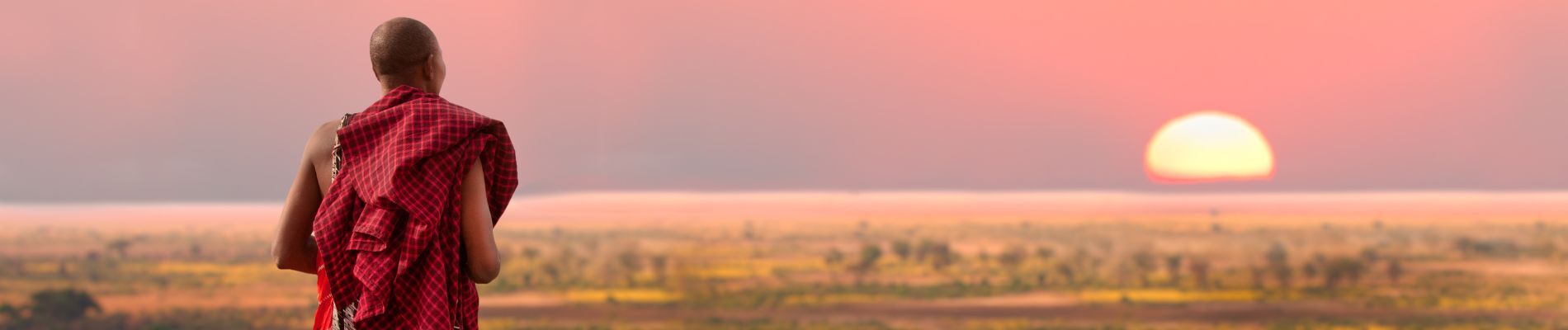 Massai blickt über weite Landschaft und in den Sonnenuntergang