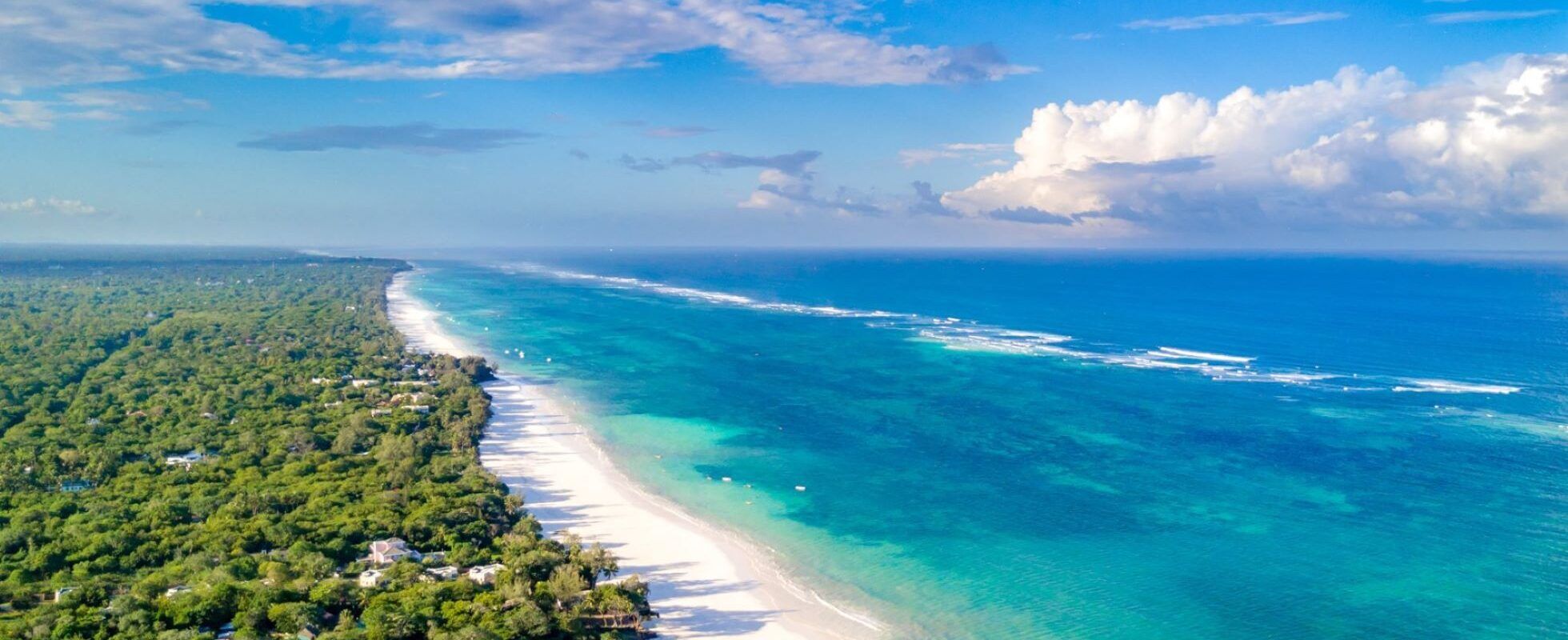 Weißer Sandstrand von Diani Beach mit Bäumen auf einer und dem blauen Meer auf der anderen Seite