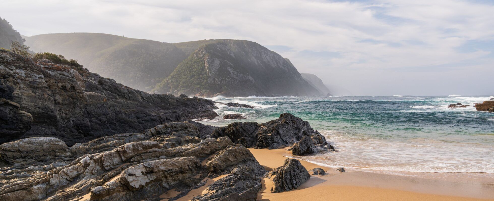 Bucht mit Sandstrand, Wellen und felsiger Küste