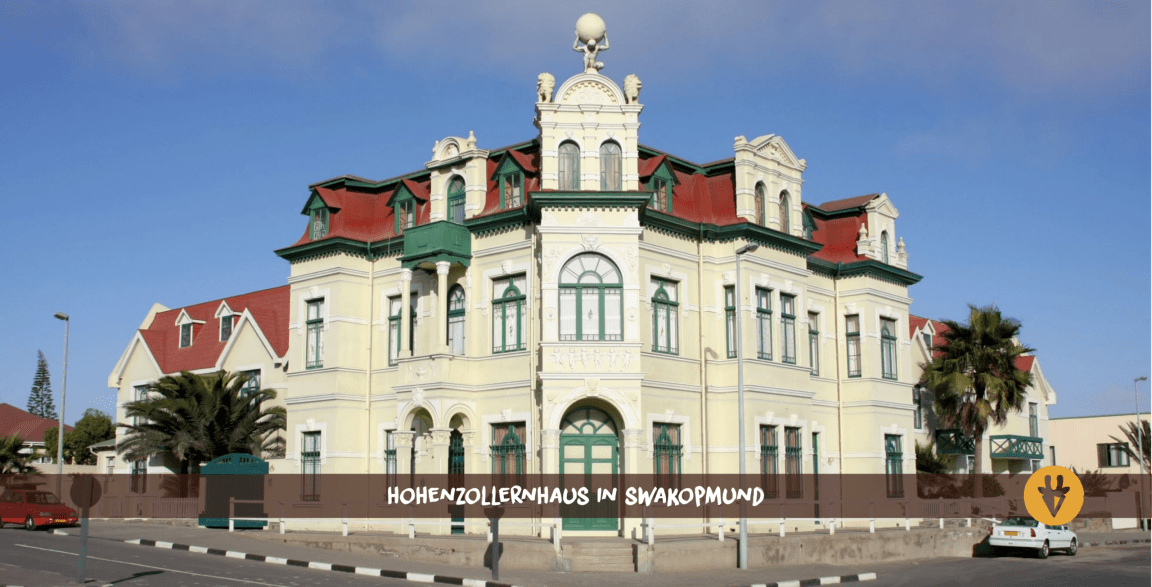 Swakopmund Hohenzollernhaus an der Ecke zweier Straßen mit zwei Autos im Vordergrund
