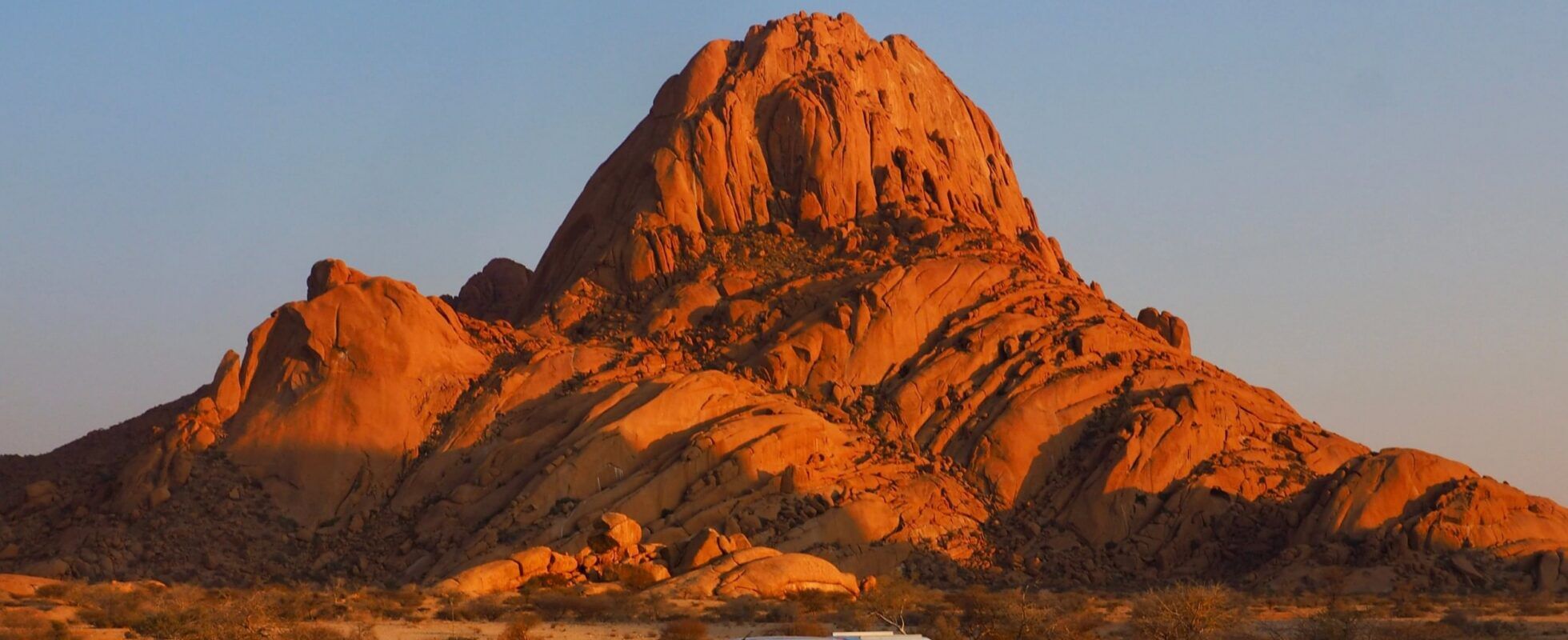 Safari-Fahrzeug parkt in Spitzkoppe vor einem hohen Felsen bei Sonnenuntergang