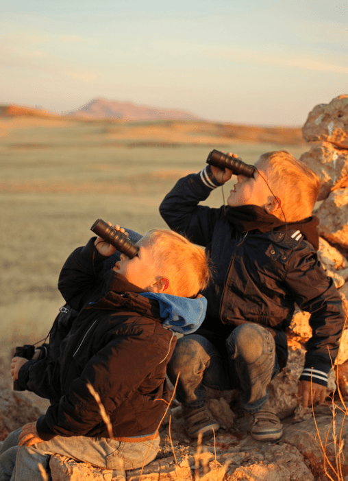 Zwei Kinder mit Fernglas auf Steinen