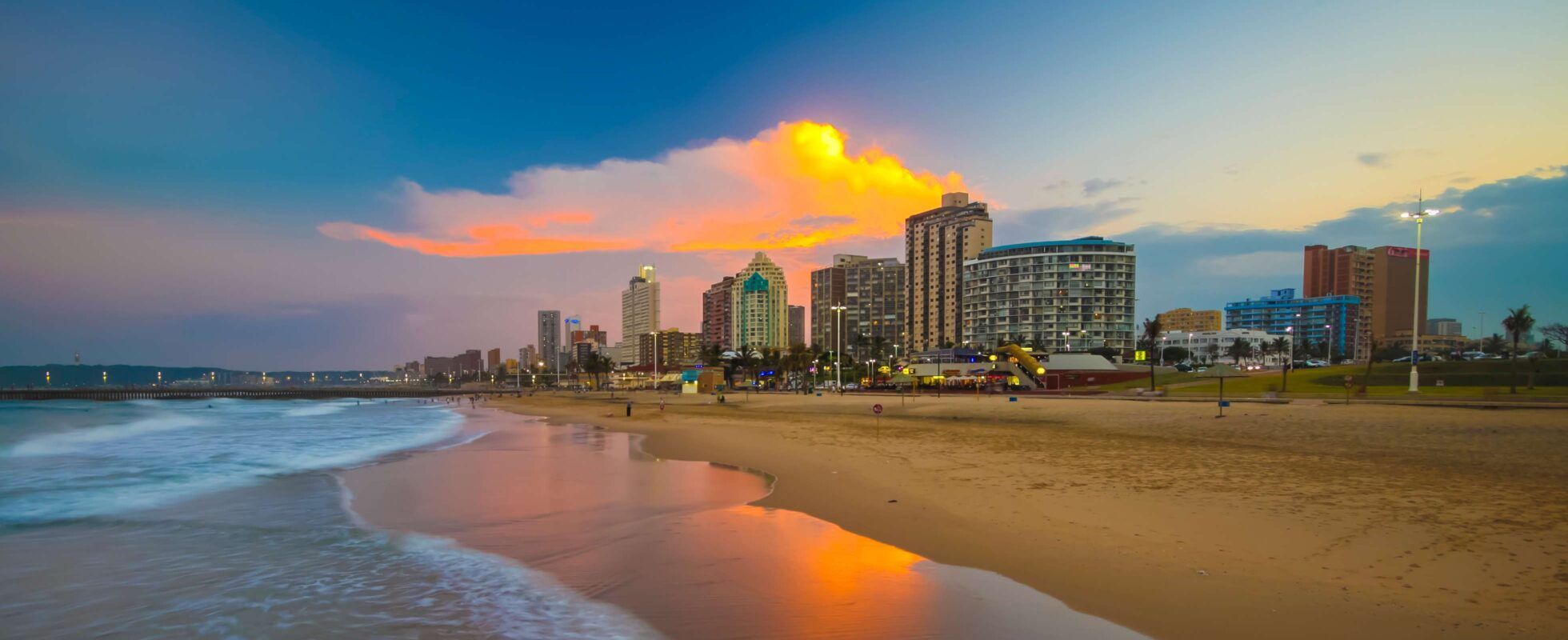 Sandstrand mit kleinen Wellen vor der Skyline von Durban bei Sonnenuntergang